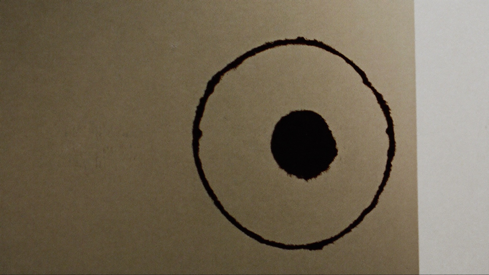 A single black ink circle brushed onto thick cream paper.